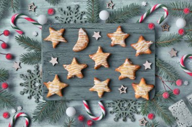 Kesme tahtasındaki el yapımı yıldız şekilli Noel kurabiyeleri, köknar dalları, böğürtlenler, pembe çizgili şeker kamışları ve yıldızlarla süslenmiş açık yeşil arka planda yatıyordu..