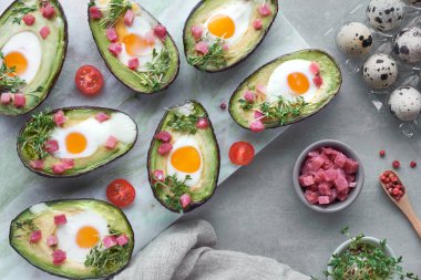 Keto diyet yemeği: Avokado tekneleri bıldırcın yumurtaları, jambon küpleri ve tereler hafif taştan servis panosunda ve etrafındaki malzemelerle birlikte.