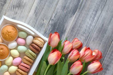 Paskalya düzlüğü turuncu laleler ve tatlılar ile döşenmiş gri ahşap desenli bir tepsi, kopyalama alanı