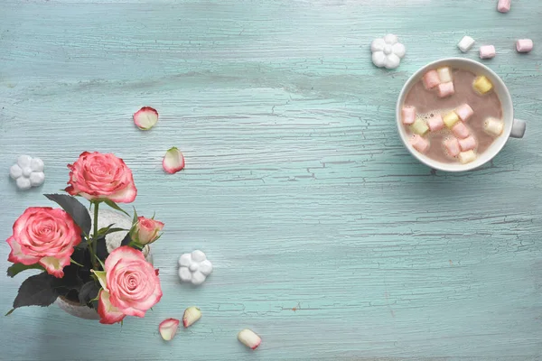 Pink roses and hot chocolate with marshmallows on light mint background with decorative ceramic flowers, flat lay with text space
