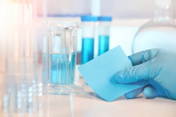 Scientific, medical or education background. Biological or biochemical lab out of focus, closeup on gloved hand holding a note. Focus on the hand. Space for your text.