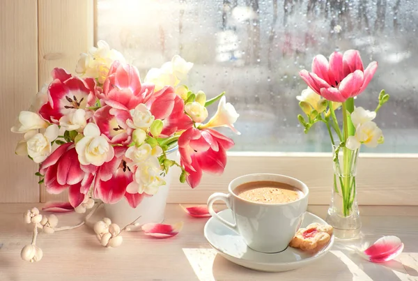 Cup of coffee  on the window board, sunshine after the rain. Spring flowers: pink tulips and white freesia.