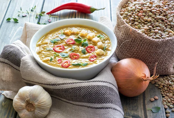 Spicy lentil soup with chili, garlic and onion on rustic wooden table. The soup is served with chili, croutons and thyme leaves. — Stock Image Spicy Lentil Soup Chili Garlic Onion Rustic Wooden Table Soup Stock Photo