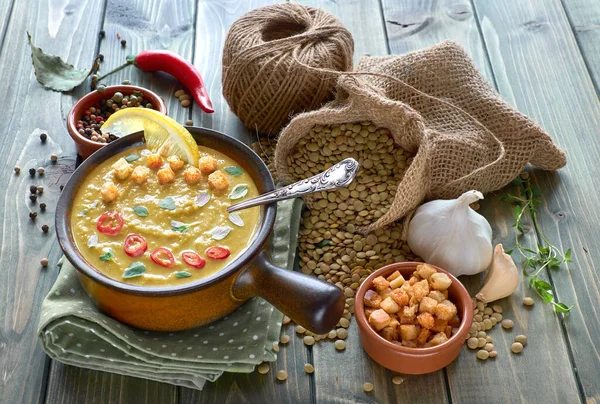 Spicy lentil soup with chili, garlic and onion, served with chili, lemon, croutons and thyme leaves in pottery ceramic bowl on the wooden table, with ingredients around the bowl — Stock Image Spicy Lentil Soup Chili Garlic Onion Served Chili Lemon Croutons Royalty Free Stock Images