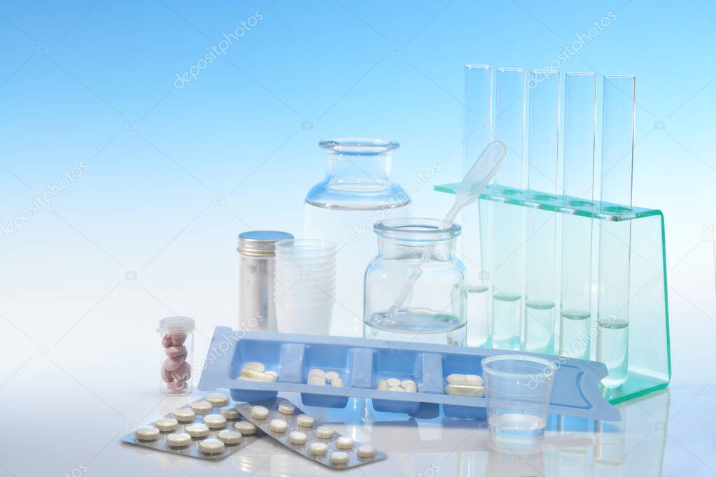 Chemical and analytical glassware and various pills on light blue gradient background, text space