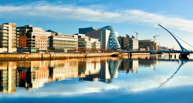 Dublin 'deki Liffey nehrindeki modern binalar ve ofisler güneşli bir günde, sağda Harp köprüsü