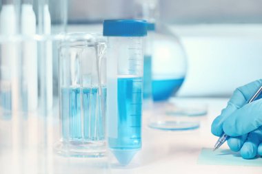 Bilimsel, tıbbi veya eğitim geçmişi. Biyolojik ya da biyokimyasal laboratuvar odak dışında, eldivenli el bir not yazma yakın çekim. Ele odaklanın