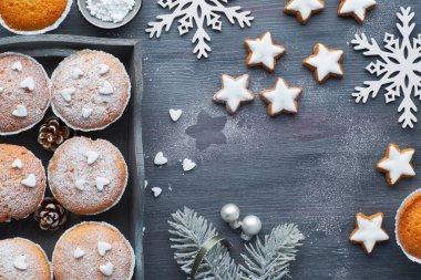 Masanın en üst manzarası şekerli kekler, şekerli krema ve koyu ahşap tahta üzerinde Noel yıldızı kurabiyeleri.