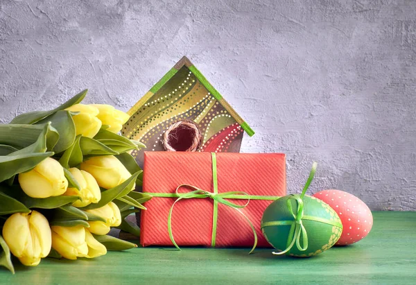 Gele tulpen, vogelhuisje en geschilderde paaseieren met ingepakte pr — Stockfoto