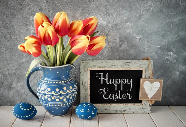 Tulipani rosso-gialli in brocca di ceramica blu con uova di Pasqua e un — Foto Stock