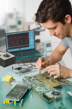 Genç enerjik erkek teknik ya da mühendis elektronik ekipman araştırma tesisinde onarır. Sığ Dof, odak alt yüzünde.