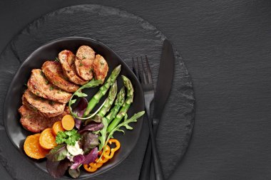 Kızarmış sığır eti, tatlı patates, kuşkonmaz ve siyah tabakta karışık yeşil salata.