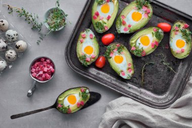 Keto diyet yemeği: jambon küplü avokado tekneleri, bıldırcın yumurtası ve tereli lahanalar, üstü gri taşın üzerinde.