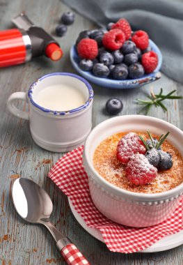 Beyaz ramekin içinde ahududu, yaban mersini ve biberiyeli creme brulee ve sade ahşap masa üzerinde yanan meşale.. 