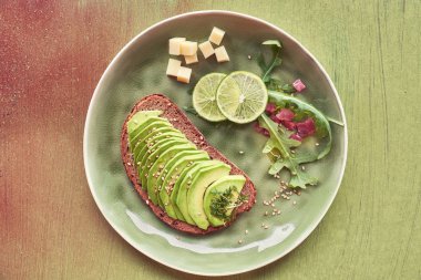 Avokado sandviçi ve kahverengi desenli arka planda jambon küplü yeşil salata.