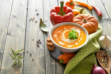 Baharatlı balkabağı çorbası fırında dolmalık biber, kırmızı soğan ve sarımsak ahşap masada, krema ve fesleğenle tatlandırılmış.. 