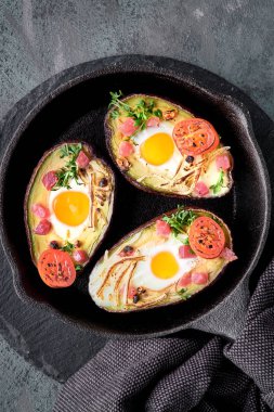 Keto diyet yemeği: jambon küplü avokado tekneleri, bıldırcın yumurtaları, peynir ve kiraz domatesleri demir tavada havluyla, üstü koyu arkaplanda.