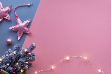 Noel düzlüğü, iki renkli pembe ve gümüş renkli kağıt üzerinde yumuşak pembe metalik tekstil yıldızları. Hafif çelenk ve mor biblolarla süslenmiş küçük yapay Xmas ağacı, metin alanı.