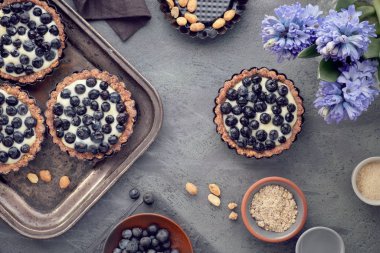 Vanilyalı böğürtlenli tartlar ve koyu arkaplanda sümbül çiçekleri.