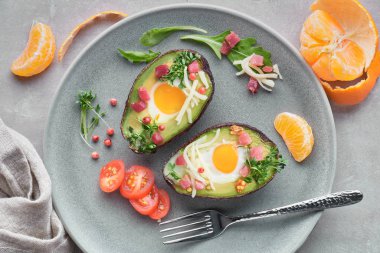 Keto diyet yemeği: jambon küplü fırında avokado tekneleri, bıldırcın yumurtası ve peynirli bıldırcın ve salata ile servis edilen gri bir masada bir içecek ve mandalina.