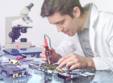 Elektronik arka plan. Genç enerjik erkek teknolojisi ya da mühendis araştırma tesisinde elektronik ekipman tamir ediyor. Sığ Dof, işçinin ellerine odaklan. Bu resim tonlandırılmış.