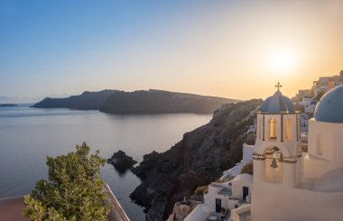 Yunanistan 'ın Santorini adasındaki Oia köyünde mavi kubbeli yerel kilisenin üzerinde gün batımı