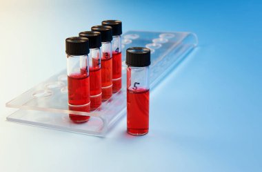 Mavi arka plandaki bir tüp standında plastik şişelerde üç sıvı örneği var.