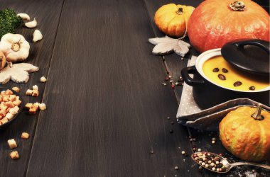 Koyu arkaplanda seramik tepside balkabağı kreması çorbası. İçindekiler: balkabağı, havuç, soğan, sarımsak, maydanoz, tuz ve biber ayrıca kızarmış ekmek ve kabak çekirdeği. Metin uzayı.