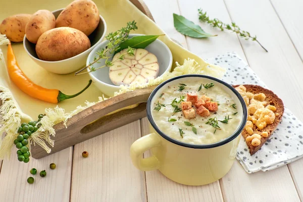 Homemade cream of potato soup in mug with croutons and thyme, served with bread toasted with cheese on light wooden table