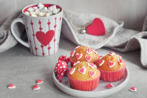 Muffins decorated with sugar hearts and a cup with red heart on light gray background. Valentine's day or winter birthday concept.