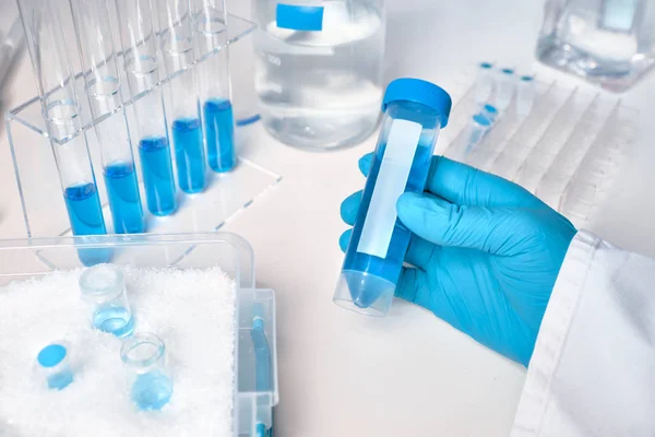 白色和蓝色的科学背景 戴手套母手中的液体样品 玻璃和塑料管中的蓝色液体样品 — 图库照片
