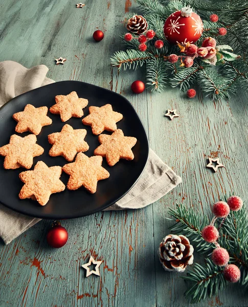 Rustic Christmas background in green and red. Star-shaped cookies on black plate with Xmas decorations. Toned image.