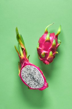 Taze organik ejderha meyvesi (pitaya veya pitahaya) yeşil naneli arka planda ikiye bölünmüştür. Canlı pembe ve yeşil renkli egzotik meyvelerle yaratıcı düz bir düzen..