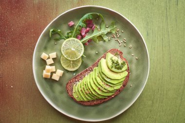 Avokado sandviçi ve kahverengi desenli arka planda jambon küplü yeşil salata.