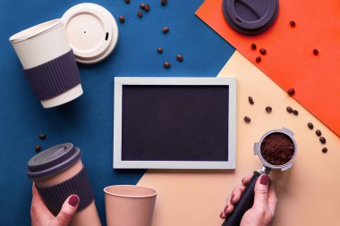 Kahve ziyanı yok. Ellerinde çevre dostu yeniden kullanılabilir kahve fincanları, hayali mavi, krema ve lüle rengi tonlarında bölünmüş kağıt üzerinde geometrik üst görünüm, tebeşir tahtasında kopyalama alanı.