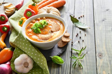 Baharatlı sebze çorbası fırında dolma biber, domates, havuç, kırmızı soğan, sarımsak ve zencefil, ahşap masada. Çorba krema, kızarmış ekmek ve maydanozla tatlandırılmış. Metnin için boşluk.