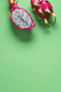 Yeşil nane arkaplanından taze organik ejderha meyvesi (pitaya veya pitahaya) kesilir. Fotokopi alanı olan yaratıcı düz bir düzen. Canlı pembe ve yeşil renkli egzotik meyveler ikiye bölünmüş..