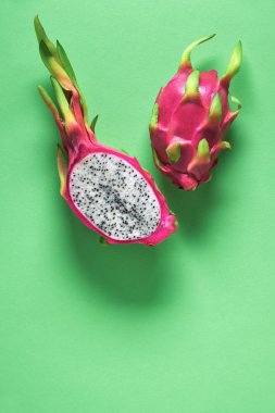 Yeşil nane arkaplanından taze organik ejderha meyvesi (pitaya veya pitahaya) kesilir. Fotokopi alanı olan yaratıcı düz bir düzen. Renkli egzotik meyveler canlı pembe ve yeşil, bir bütün ve ikiye bölünmüş..