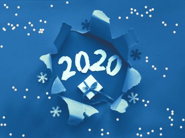 Trnedy klasik mavi renkli kağıt düz yerde kar taneleri ve ortasında yırtık bir delik vardı. Yeni yıl hediyesi ve delikte 2020 numaralı kağıt var. Mutlu yıllar 2020!