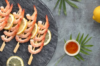 Lezzetli limon ve sarımsaklı karides ahşap çubuklarda, düz uzanmış koyu taş arka planda