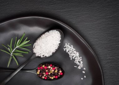 Siyah tabakta siyah kaşıklarda siyah kayrak zemin üzerinde tuz ve karışık biber.