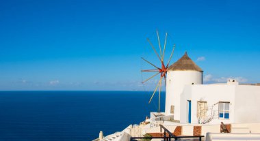 Yunanistan 'da güzel Santorini - Oia köyünde geleneksel yel değirmeni ve apartmanlar güneşli bir günde, panoramik görüntü.