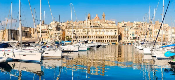 Grand Bay, Valetta, Malta 'da Senglea marinasında yelkenli sürerken güneşli bir sabahta modern sahil restoranları ve histoik binalar tarafından Birgu' daki süper marinanın panoramik görüntüsü.
