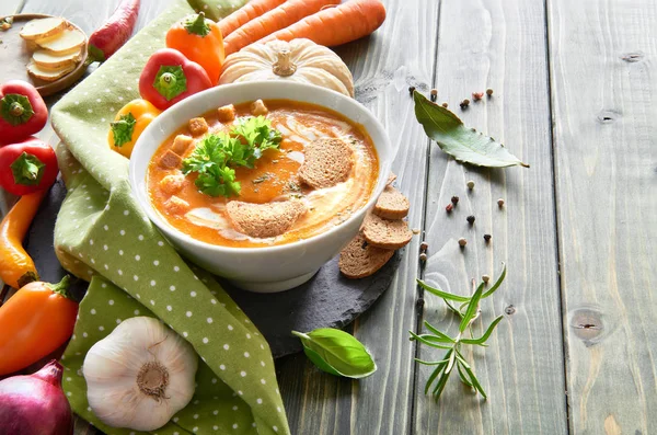 Baharatlı sebze çorbası fırında dolma biber, domates, havuç, kırmızı soğan, sarımsak ve zencefil, ahşap masada. Çorba krema, kızarmış ekmek ve maydanozla tatlandırılmış. Metnin için boşluk.