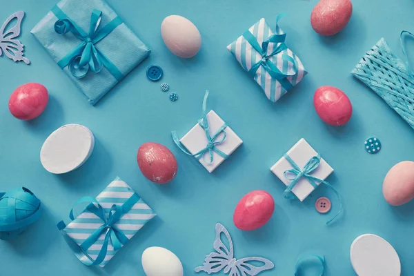 Paskalya dairesi mavi nane arkaplanda beyaz ve pembe olarak yatıyordu. Renkli yumurtalar, hediye kutuları ve bahar dekorasyonlarıyla geometrik desen.