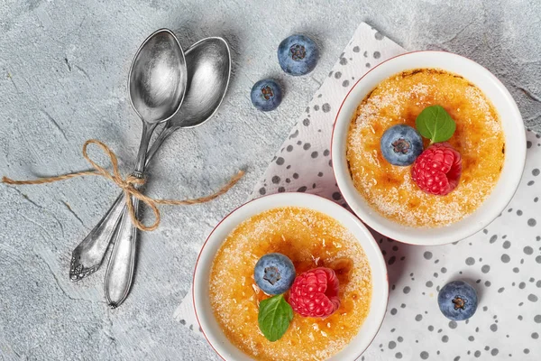 Creme brulee (krema brulee, yanmış krema) kaseleri ahududu, yaban mersini ve nane ile süslenmiş açık beton, düz uzanmış