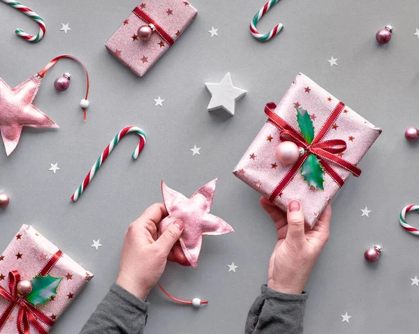 Festive toned two tone Christmas background with pink gift boxes, stripy candy canes, trinkets and decorative stars, geometric creative flat lay on silver paper in pink, magenta and green.