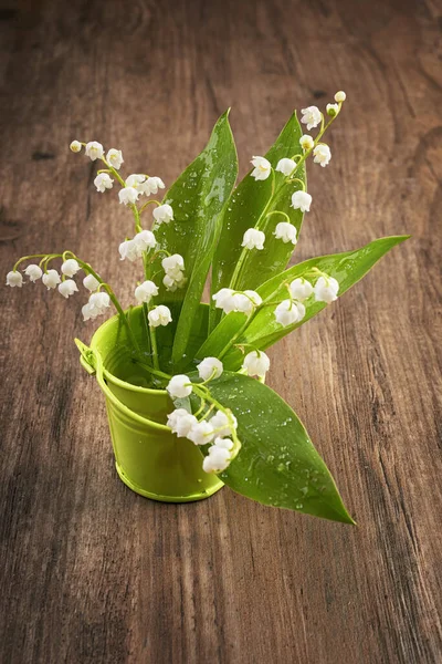 loseup on lily of the valley flowers in small green basket on wood