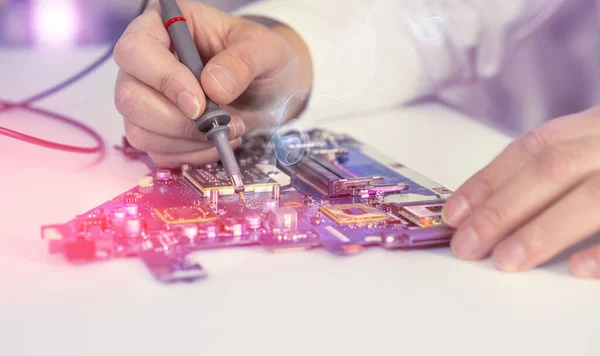 Electronics repair service, hands of female tech fixes an electronic circuit. Shallow DOF, focus on the tip of the test device and part of the hand. This image is toned.