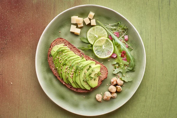 Avokado sandviçi ve kahverengi desenli arka planda jambon küplü yeşil salata.